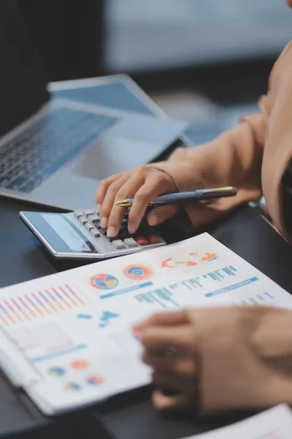 Análisis financiero: manos sobre una calculadora, junto a un informe con gráficos y una notebook.